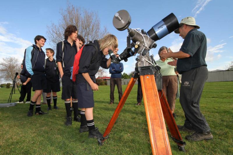 School children looking through a telescope in a field